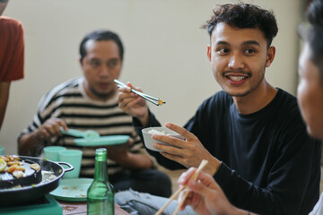 Cheerful Young Man Talking With Friends While Eating Barbecue Grill Using Chopstick At Restaurant