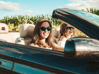 Portrait of two young beautiful and smiling hipster female in convertible car. Carefree women...