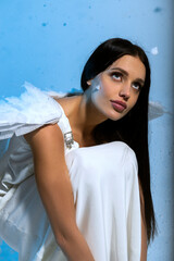 Studio portrait of sexy blonde in white long elegant dress and angel wings, she poses sensually 