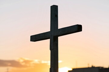 A photo of a wooden cross silhouette against a bright orange sky.