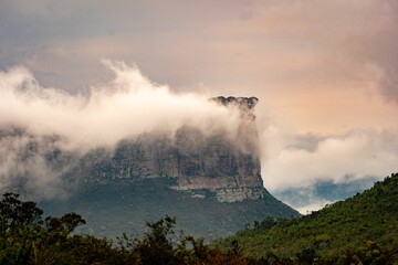 Majestic mountain peak shrouded in clouds with lush greenery in the foreground.