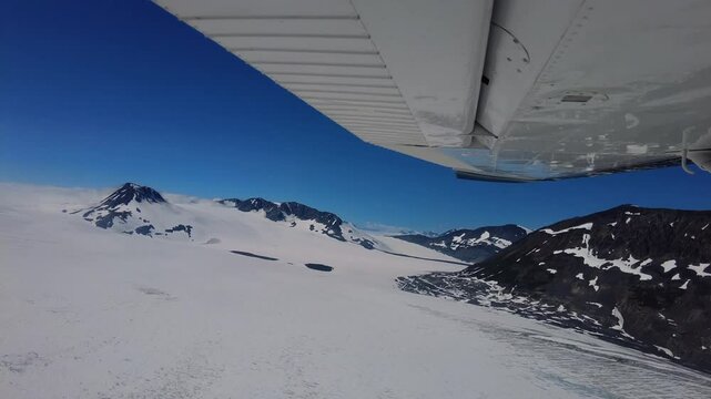 View of Harding Icefield with airplane's wing in the frame, showcasing cliffs, snow and blue sky