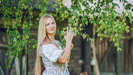 Blond haired female in authentic slavic attire caressing birch foliage amid rural landscape, connecting with cultural roots