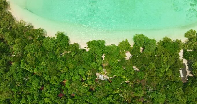 A breathtaking aerial view of a secluded Mai Ngam beach with crystal-clear turquoise waters, surrounded by lush green vegetation and corel reef. The pristine white sand and vibrant ocean hues