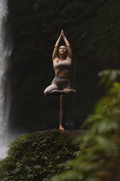 Woman practising yoga in front of waterfall on the island of Bali
