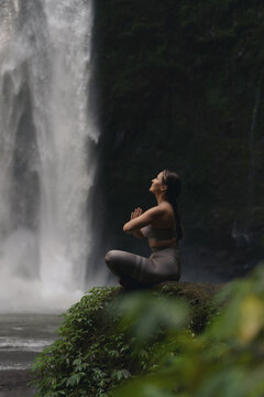 Woman practising yoga in front of waterfall on the island of Bali