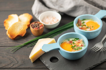 Oeuf cocotte. Baked eggs (Eggs in cocotte) with сheese, bacon and green onion in portion ceramic bowl on white background. Comfort food for breakfast.