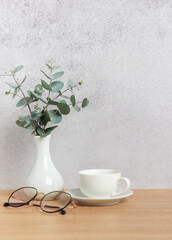 Eucalyptus branches, coffee cup and eyeglasses resting on wooden desk