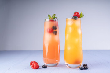refreshing citrus and berry cocktails with mint garnish in tall glasses against a minimalistic backdrop, highlighting vibrant orange and pink hues amid scattered fresh raspberries and blueberries.