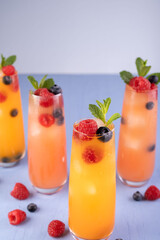 vibrant summer mocktails in tall glasses with fresh berries and mint, showcasing a refreshing blend of vivid orange and red hues on a soft lavender surface. party, vivid, relaxing, serving, chilled