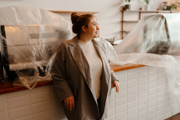 A Caucasian adult businesswoman with brown hair tied in a bun dressed in a gray blazer standing in...