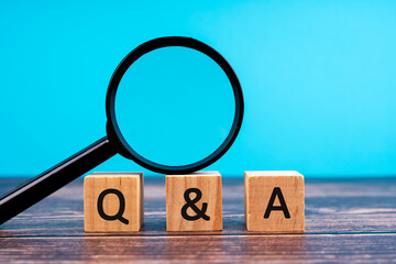 Q and A written on wooden blocks with magnifying glass on wooden table