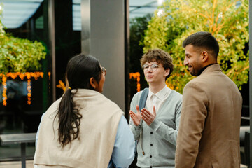 A young White man in his late 20s, talking to his colleagues, a young Indian woman, and an older...
