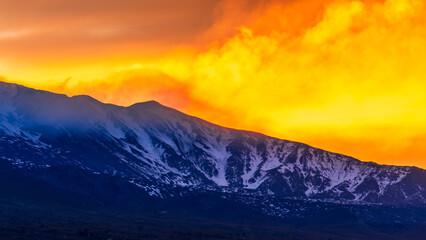 beautiful orange mountain sunset with highland slope in snow and amazing cloden eveninf clouds on background