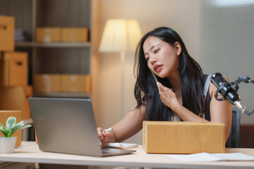 Young asian woman managing online sales and logistics, talking on the phone, taking notes on a laptop, and preparing packages in a home office
