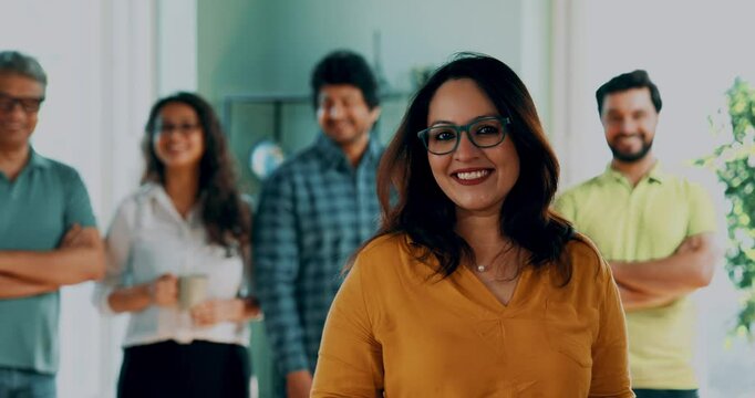 Indian Asian young male entrepreneur in smart casual wear confidently looking at camera, her happy startup team standing together behind, modern corporate office, leadership, success and growth