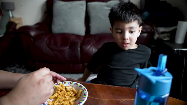 Parent offering pasta to a toddler who is refusing to eat at home, highlighting the challenges of mealtime with a picky eater