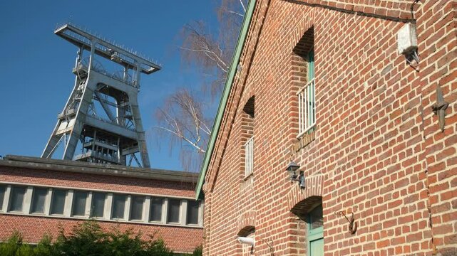 The Wallers-Arenberg coal mine features a historic red brick building and a metal headframe under a clear blue sky, showcasing France&rsquo;s industrial heritage. Tilt shot.