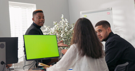 A smiling male manager discusses work strategies with his co-workers. He leans over the desk, explains something, motivates his team to action, and conducts conferences and training sessions.