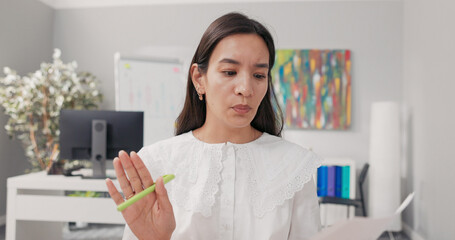 The accountant, sitting in the office, speaks with the boss through a video call. He asks about the details of the contract, holding up documents and pointing to them, worried about the accuracy.