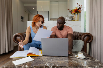 Couple discussing documents in the living room with a laptop and coffee