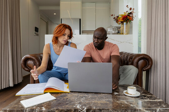 Couple discussing documents in the living room with a laptop and coffee