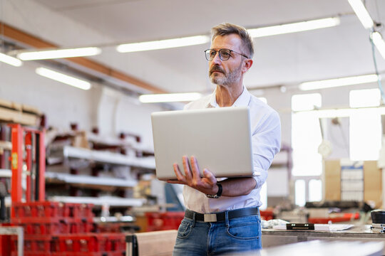 Man in a production hall holding a laptop in an industrial setting