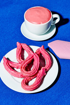 Pink churros and pink hot chocolate on a blue table