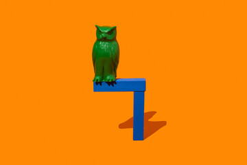 Green owl toy perched on a blue stand against an orange background