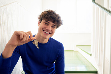 Young man at home holding keys, symbolizing moving into a new flat