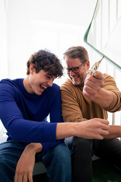 Father and son laughing together at home with keys to a new flat