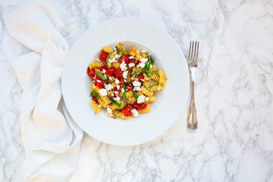 Fusilli pasta with tomatoes, feta cheese, and pine nuts on a marble background