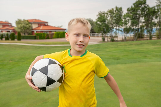 Smiling boy holding a football on a green field - Powered by Adobe