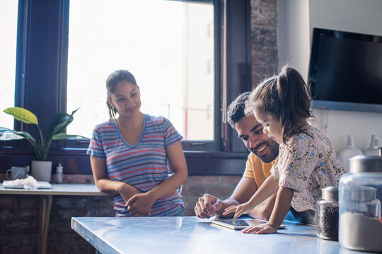 Family sitting in kitchen, father using digital tablet with daughter