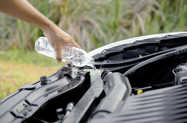 Driver's hand pouring or refilling water into the windshield washer tank inside the car hood. Checking and refilling the car's radiator.