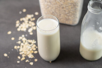 A glass of oat milk and oatmeal in a box on grey kitchen table. Vegan and non-dairy alternative milk