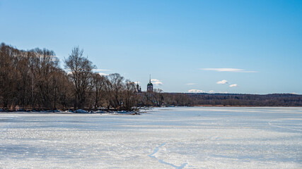 Fototapeta premium The lake shore with frozen water, bare trees in sunny day at early spring. 