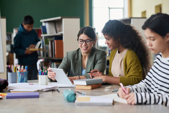 Cheerful teacher helping students with a tablet in a classroom setting