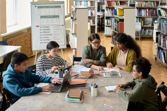 Young students learning grammar with teacher at desk in group class
