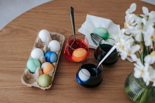 Easter eggs being dyed on a wooden table with flowers and tools