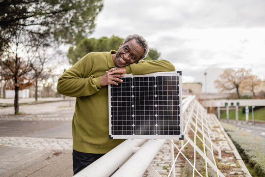 Man smiling and leaning on a solar panel outdoors in an urban setting