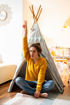 Young woman sitting in a cosy home setting, making a peace sign in front of a tipi tent