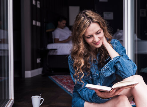 Woman reading a book at home in the morning with a man in the background