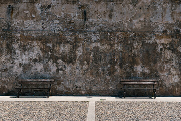 Two empty benches next to the old shabby wall