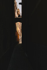 Dark narrow passage between buildings with a sunny street in the end