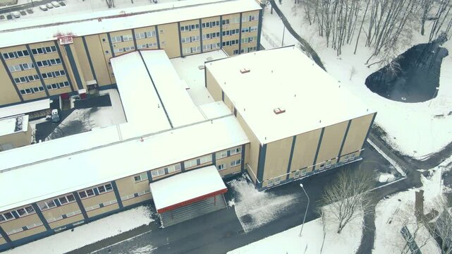 Aerial drone footage of a Schoo during winter time named Tallinn Tehnika G&uuml;mnaasium or high school during a cloudy dat with white snow around anr on the roof. Tall trees are surrounding in Mustam&auml;e.