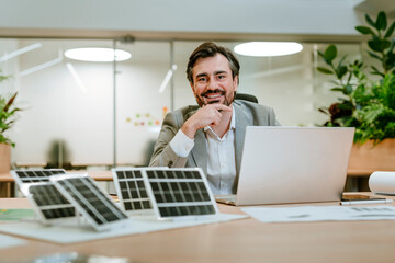 Businessman in office with solar panels and laptop promoting sustainability