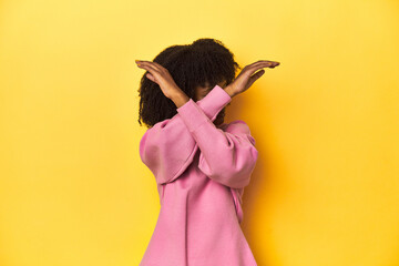 Teen girl in pink sweatshirt, yellow studio backdrop keeping two arms crossed, denial concept.