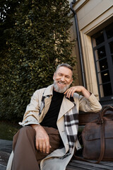 A sophisticated senior man exudes charm while seated casually on a bench.