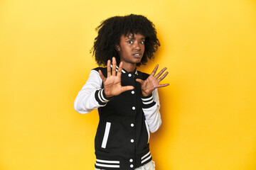 Obraz premium Teen girl in baseball jacket, yellow studio background being shocked due to an imminent danger